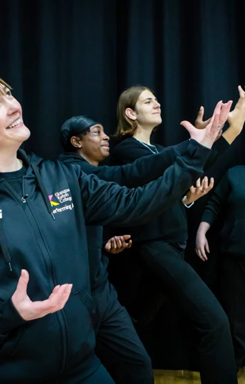 A lecturer and students striking dramatic poses against a black curtain, smiling and enjoying their creative acting activity. A lecturer and students striking dramatic poses against a black curtain, smiling and enjoying their creative acting activity.